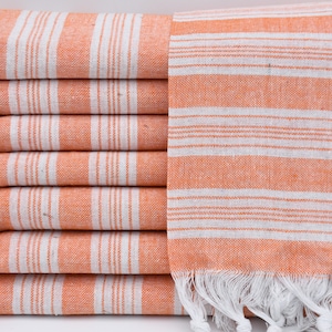 May include: A stack of orange and white striped towels with white fringe. The towels are made of cotton and are soft and absorbent.