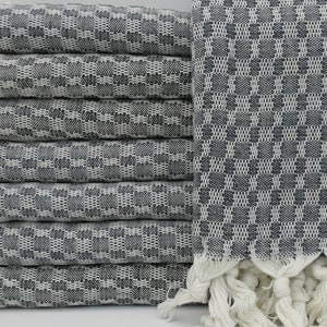 May include: A stack of white Turkish towels with a black and white checkered pattern. The towels have fringe on the ends.