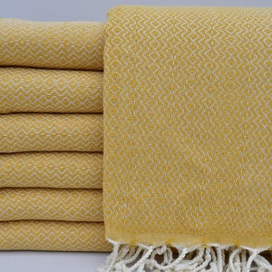 May include: A stack of yellow Turkish towels with white fringe. The towels have a diamond pattern.