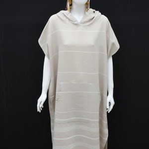 May include: A beige hooded towel with white stripes and a pocket. The towel has fringe at the bottom.