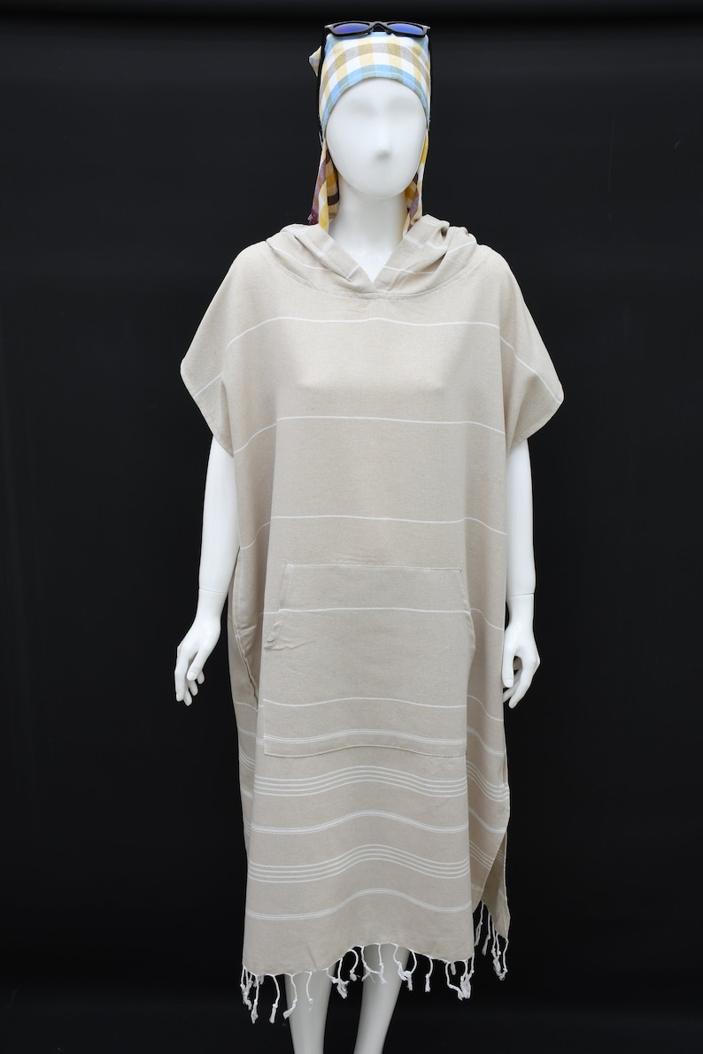May include: A beige hooded towel with white stripes and a pocket. The towel has fringe at the bottom.