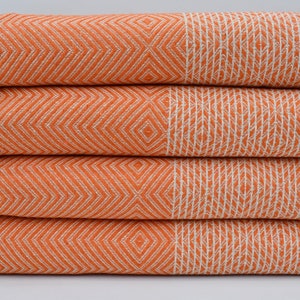 May include: A stack of four orange and white patterned Turkish towels with fringe edges.