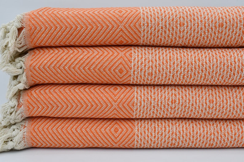 May include: A stack of four orange and white patterned Turkish towels with fringe edges.