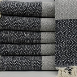 May include: A stack of five black and white patterned Turkish towels with white fringe. The towels are folded in half and stacked on top of each other.