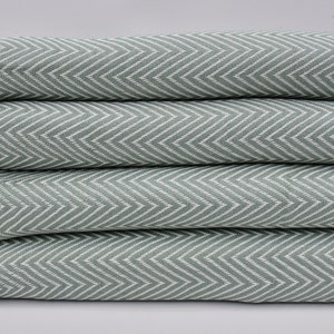 Puede incluir: Una pila de cuatro toallas de color verde y blanco con patrón de chevron y flecos blancos.
