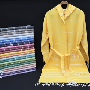 May include: A stack of colorful striped towels with fringed edges, next to a yellow hooded bathrobe with white stripes and a white tie belt.