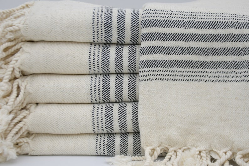 May include: A stack of white towels with black stripes and fringe. The towels are folded and stacked on top of each other.
