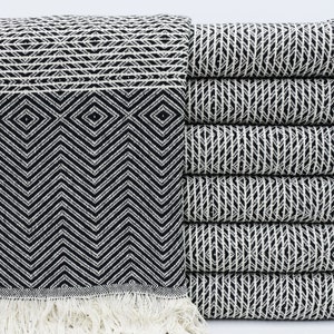 May include: A stack of black and white patterned Turkish towels with fringe. The towels are folded and stacked on a white surface.