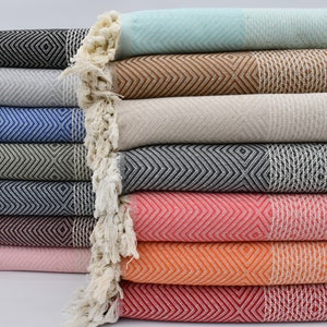 May include: A stack of ten colorful Turkish towels with fringe edges. The towels are folded and arranged in a neat pile. The towels are made of cotton and have a variety of geometric patterns.