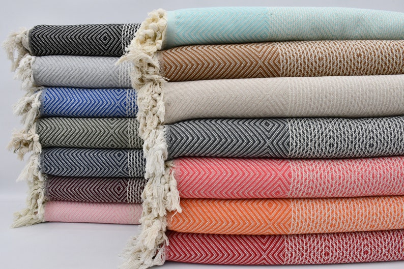 May include: A stack of ten colorful Turkish towels with fringe edges. The towels are folded and arranged in a neat pile. The towels are made of cotton and have a variety of geometric patterns.