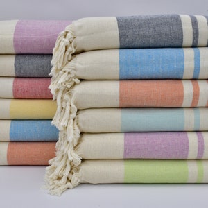 May include: A stack of striped towels in various colors, including light blue, yellow, orange, and purple. The towels are folded and have fringe edges.