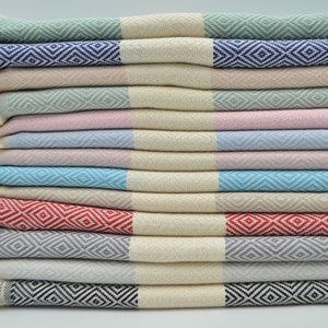 May include: A stack of ten Turkish towels in various colors, including green, pink, blue, red, gray, and black. Each towel has a diamond pattern woven into the fabric.