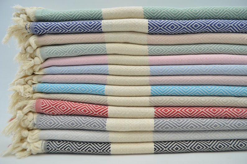 May include: A stack of ten Turkish towels in various colors, including green, pink, blue, red, gray, and black. Each towel has a diamond pattern woven into the fabric.