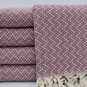 May include: A stack of five pink and white patterned Turkish towels with fringe. The towels are folded and stacked on a white surface.