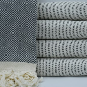 May include: A stack of four white Turkish towels with black geometric patterns. The top towel has a diamond pattern, while the other three towels have a small dot pattern.