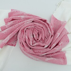 May include: A pink and white patterned Turkish towel with fringed edges. The towel is folded into a spiral shape.