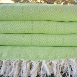 Può includere: Un set di quattro coperte in cotone verde con frange bianche. Le coperte hanno un motivo a spina di pesce.