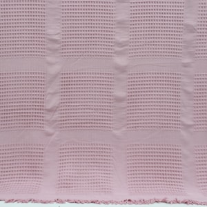 May include: A pink waffle weave throw blanket with a textured surface. The blanket is folded and has a fringe border.