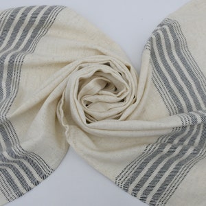 May include: A white cotton towel with black stripes. The towel is folded and has fringe on the ends.
