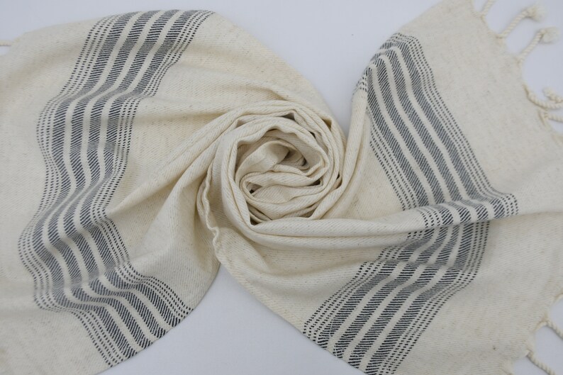 May include: A white cotton towel with black stripes. The towel is folded and has fringe on the ends.