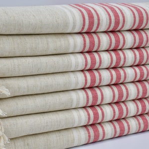 Può includere: Un mucchio di asciugamani beige con strisce rosse. Gli asciugamani hanno frange su un lato.
