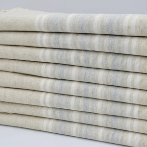 Può includere: Un mucchio di asciugamani a righe beige e blu chiaro con frange bianche.