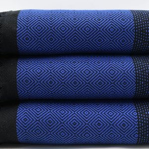 May include: Three blue and black patterned towels with fringe edges are stacked on top of each other. The towels have a diamond pattern in blue with black accents.
