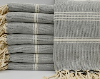May include: A stack of eight gray and white striped towels with fringe. The towels are folded and stacked on a white surface.