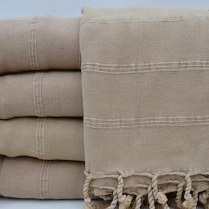 May include: A stack of four beige Turkish towels with fringe. The towels are folded and have a subtle striped pattern.
