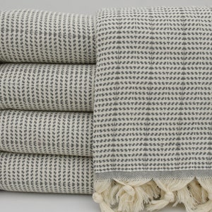 May include: A stack of four gray and white patterned Turkish towels with fringe. The towels are folded and stacked on a white surface.