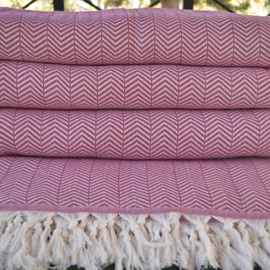 May include: A stack of four pink and white herringbone patterned throw blankets with white fringe.
