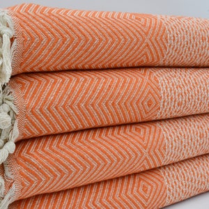 May include: A stack of orange and white patterned Turkish towels with fringe. The towels are folded and have a chevron pattern.