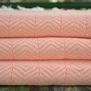 May include: A peach-colored woven throw blanket with a white chevron pattern. The blanket is folded in thirds.