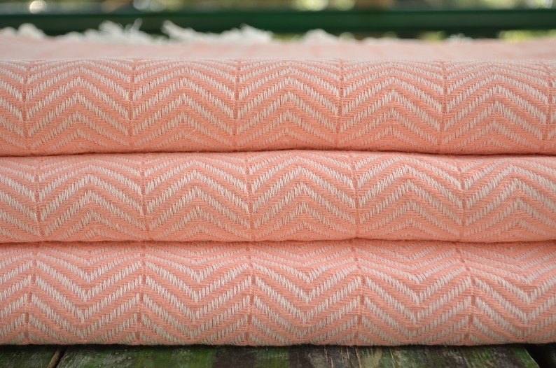 May include: A peach-colored woven throw blanket with a white chevron pattern. The blanket is folded in thirds.