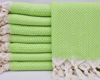 May include: A stack of green and white patterned Turkish towels with fringe. The towels are folded and stacked on a white surface.