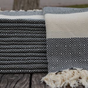 May include: A stack of black and white striped towels with a fringe border. The towels are folded and stacked on a wooden surface.