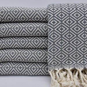 May include: A stack of six grey and white patterned Turkish towels with white fringe. The towels have a diamond pattern.