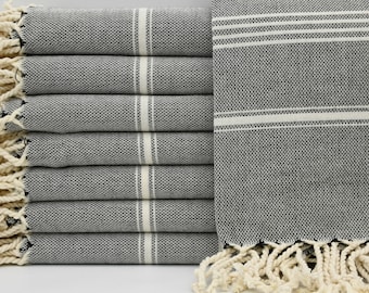 May include: A stack of black and white striped Turkish towels with fringe. The towels are folded and stacked on a white surface.