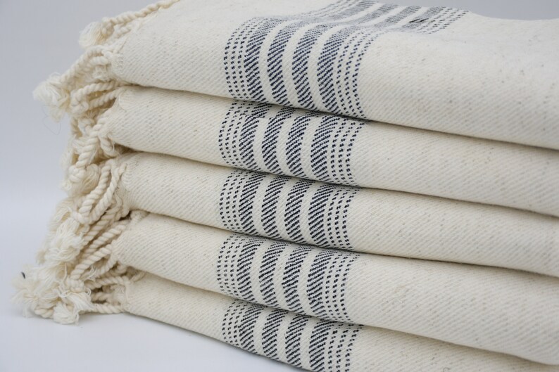 May include: A stack of five white towels with blue stripes. The towels have a fringe border.