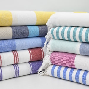 May include: A stack of colorful striped towels with fringed edges. The towels are folded and arranged in a pyramid shape. The colors include yellow, blue, green, pink, and white.