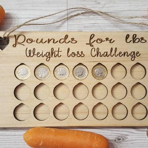 May include: Wooden weight loss challenge board with the text "Pounds for lbs Weight loss Challenge". The board has 24 slots for coins, with 6 coins already in place.