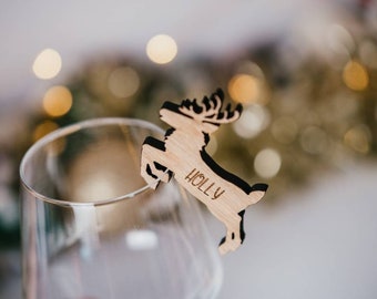 May include: Wooden reindeer Christmas ornament with the name "Holly" engraved on it. The ornament is hanging from a glass wine glass.