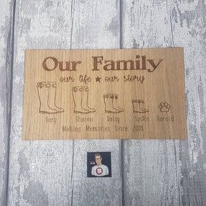 May include: A wooden sign with the text "Our Family our life our story" and a paw print. Below the text are four pairs of boots and the names Gary, Sharon, Daisy, Spike, and Harold. The sign also says "Making Memories Since 2008".