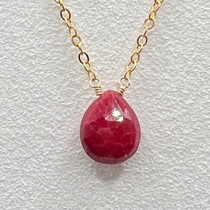 May include: A gold chain necklace with a red gemstone pendant. The pendant is a teardrop shape and has a faceted surface.