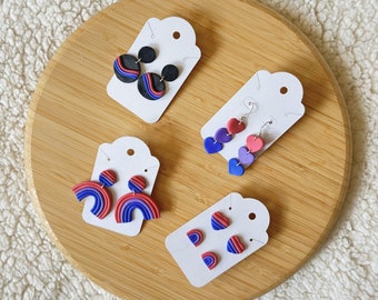 May include: Four earring cards with different styles of earrings. The earrings are made of polymer clay and feature a variety of colors, including red, blue, and black. The earrings are displayed on white cards with black text.