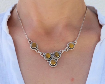 Puede incluir: Un collar de plata con un grupo de cinco piedras redondas de ojo de tigre. Las piedras están engastadas en engastes de plata y están conectadas por una cadena de plata.
