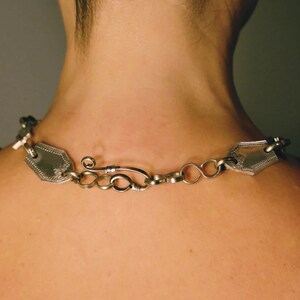 Puede incluir: Un collar de plata con una cadena y dos colgantes decorativos. El collar est&aacute; hecho de cubiertos reciclados.