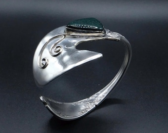 Puede incluir: Un brazalete de puño plateado hecho a mano con una piedra preciosa verde oscuro. El brazalete presenta un diseño único, que incorpora remolinos decorativos y una forma de cuchara. El diseño abierto facilita su uso.