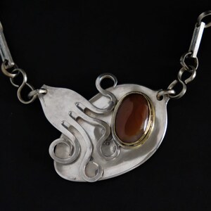 Puede incluir: Collar de plata con una piedra marr&oacute;n engastada en un bisel de oro. El colgante tiene forma de pulpo con tent&aacute;culos rizados.