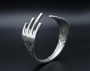 Puede incluir: Un brazalete de plata hecho a partir de un tenedor reutilizado, con forma de mano haciendo el dedo medio.